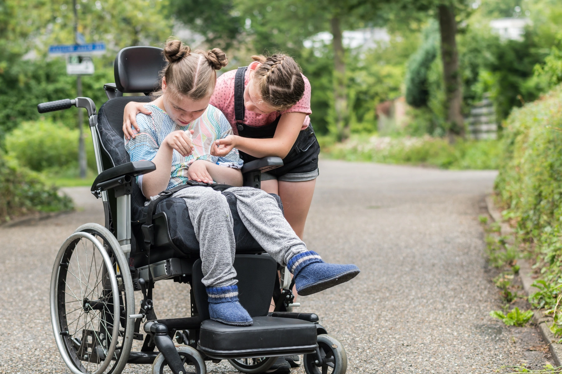 A young girl helping her disabled sister in a wheelchair