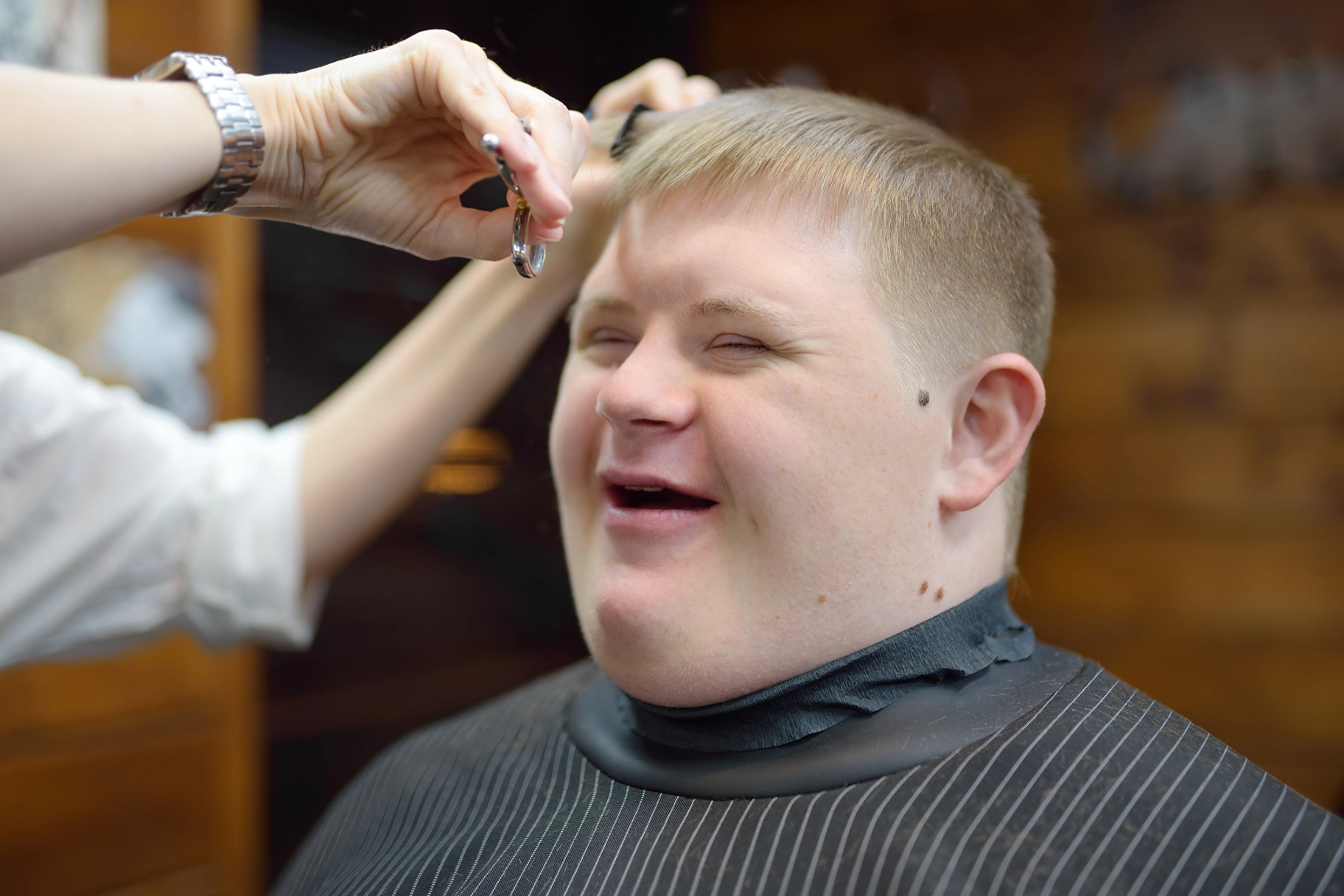 Portrait of a teenager with Down syndrome in a barbershop. The boy with Down syndrome smiles during a haircut
